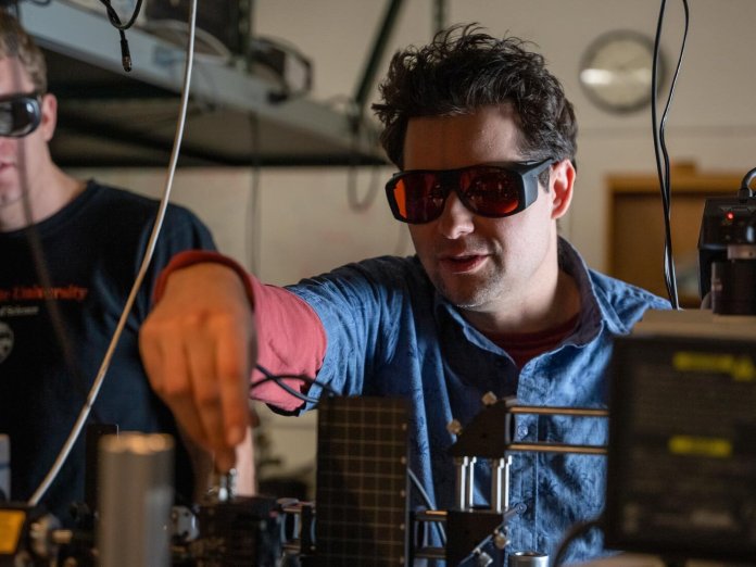 A man works in a laboratory with lazers and glasses.
