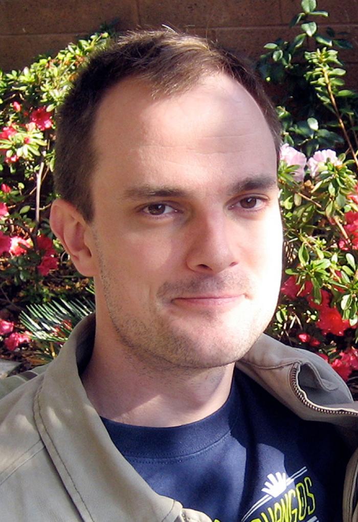 Man smiling in front of a bush of flowering azaleas