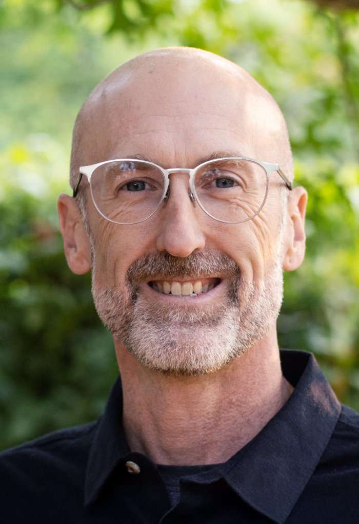 A headshot of a man in front of green plants
