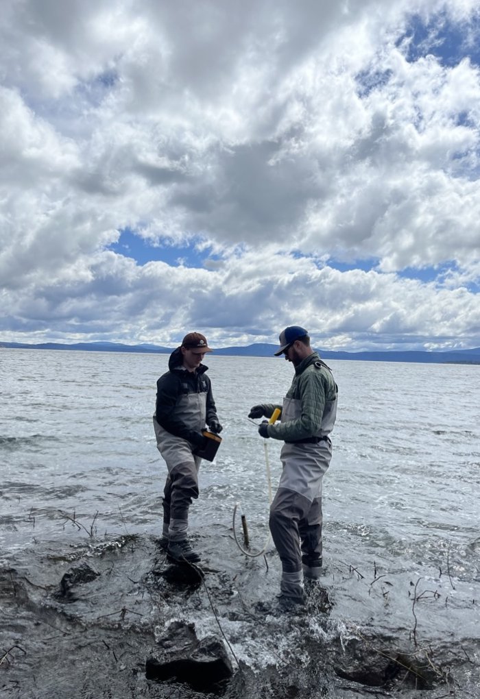 Two men in water pants collect samples in a lake.