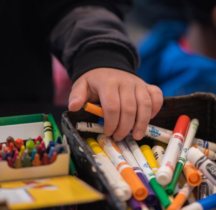 child grabbing crayons and markers from basket