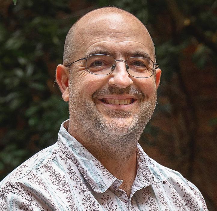 Dee Denver sitting in front of shrubbery.