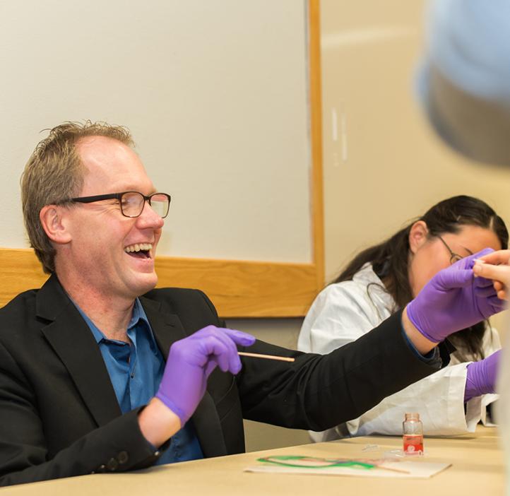 Roy Haggerty wearing gloves and laughing at a table