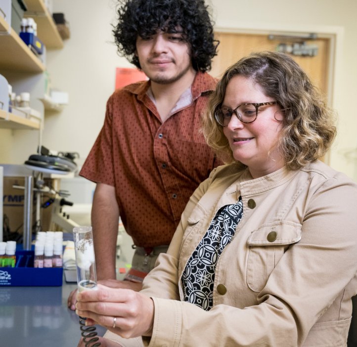 Alysia Vrailas-Mortimer sits at a lab table showing equipment to a student.