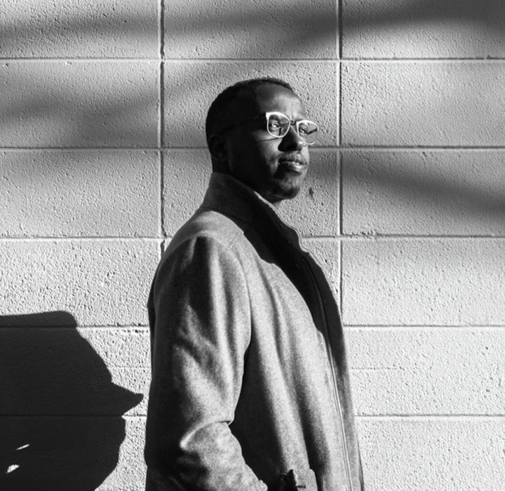 Abdikani Omar Farah stands in front of a wall in a black and white image.