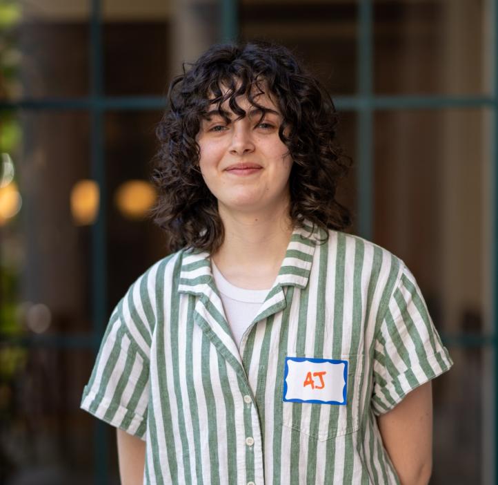 AJ Damiana wears a striped button-up with a smile, her dark, curly hair falling to her shoulders.