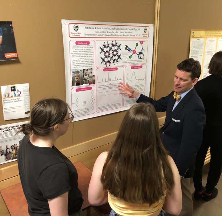 A student shows a group of people a research poster hanging on a wall.