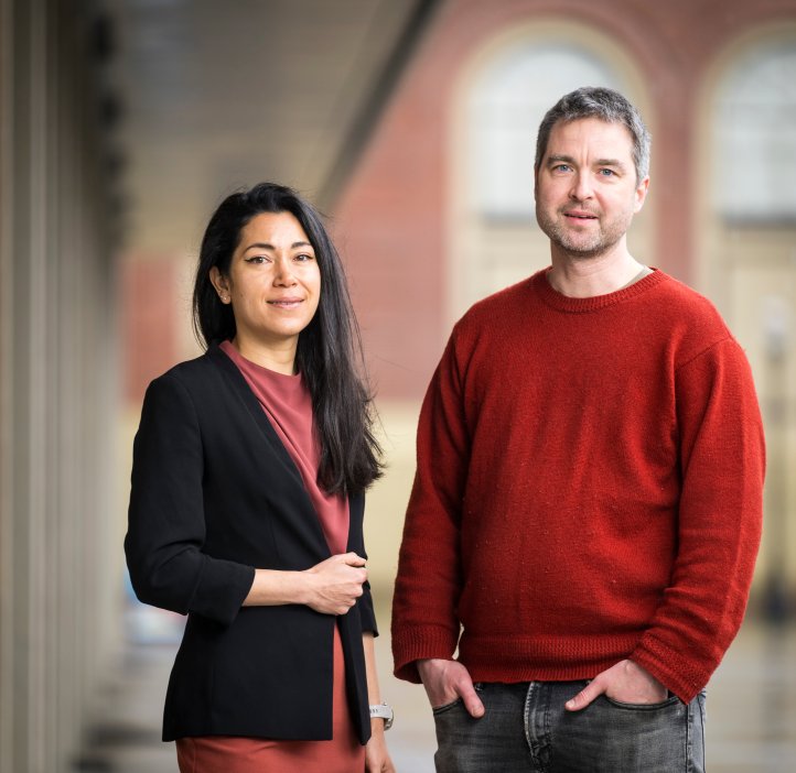 Two people stand in front of buildings.