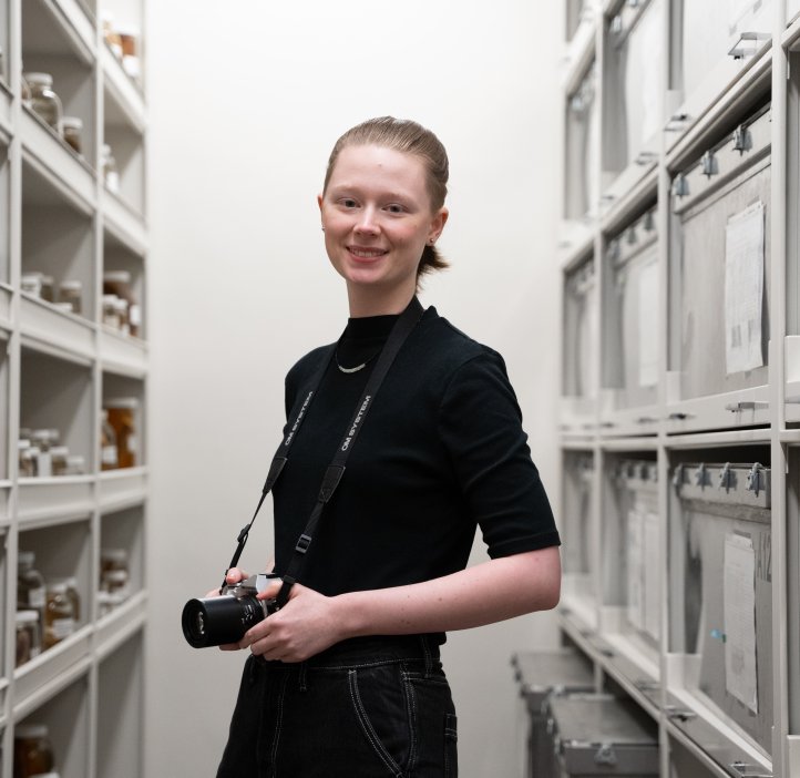 A woman in all black holds a camera in a laboratory.