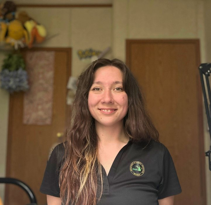A woman in a black shirt and brown hair sits at a desk.