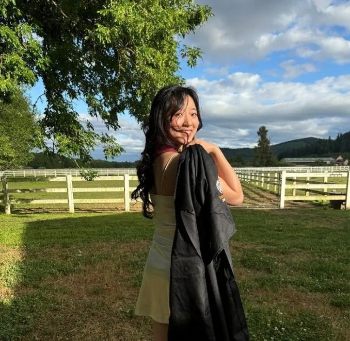 A woman in a dress holds a graduation gown.