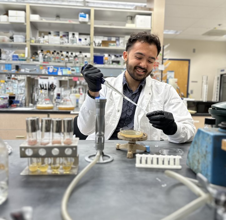 A man in lab coat and gloves uses a pipet.