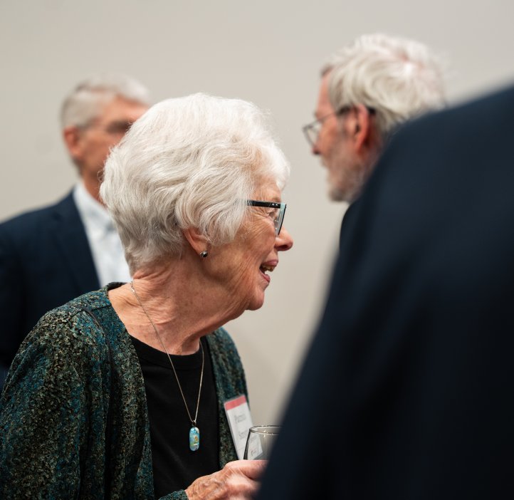 An older woman with white hair holding a glass smiles.