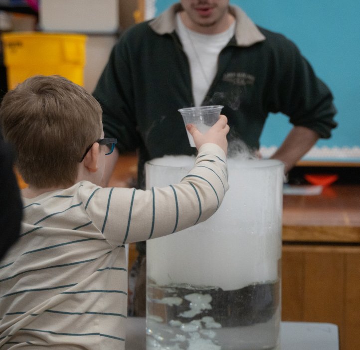 a child holds a cup over a large tub of dry ice
