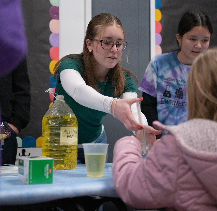 An OSU student helps a child with a syringe of colorful liquid