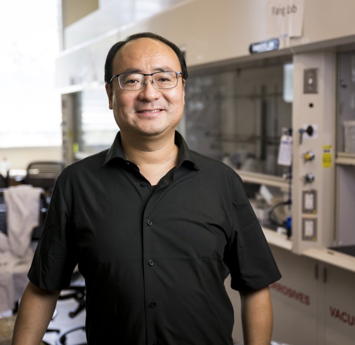 A man in a short sleeve black shirt smiles while standing in a laboratory. 