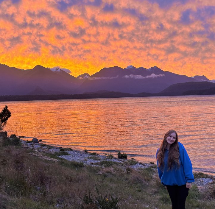 A woman stands in front of a sunset.