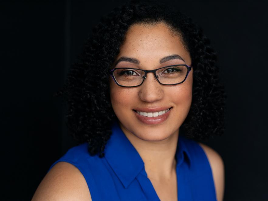 Samantha Lewis in a blue shirt and glasses with dark background