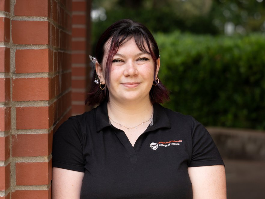Peer advisor Gwen leaning on a brick building and smiling