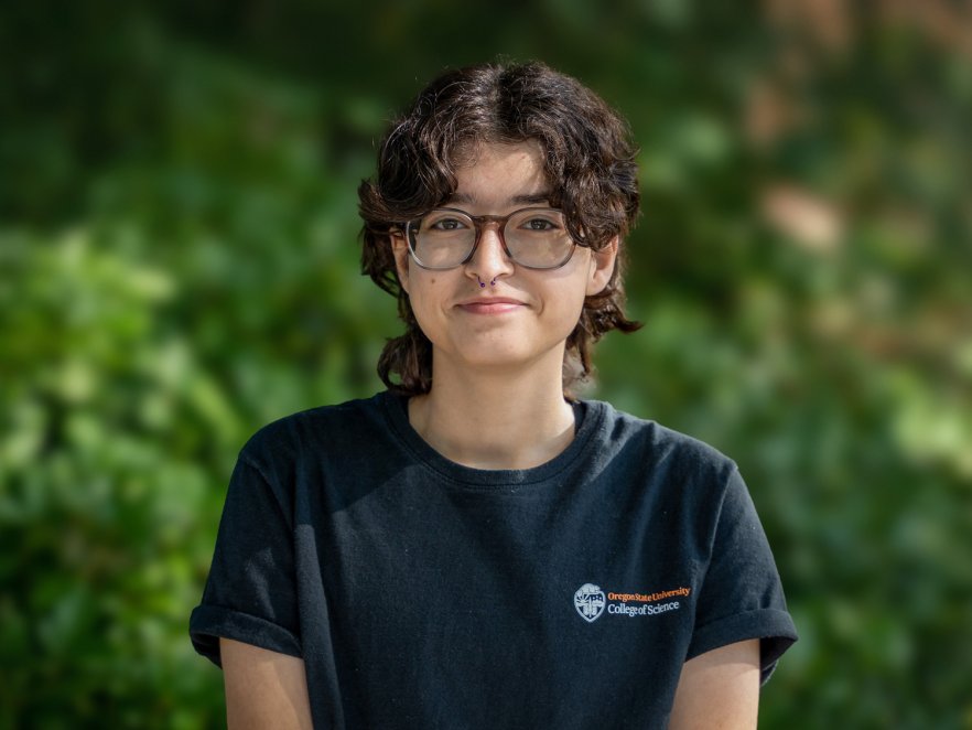 Peer advisor Milo smiles in their peer advisor shirt outside Kidder