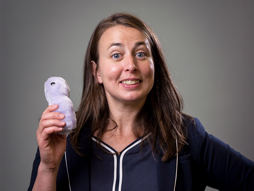 Maude David smiles in a headshot, holding a fluffy stuffed microbe