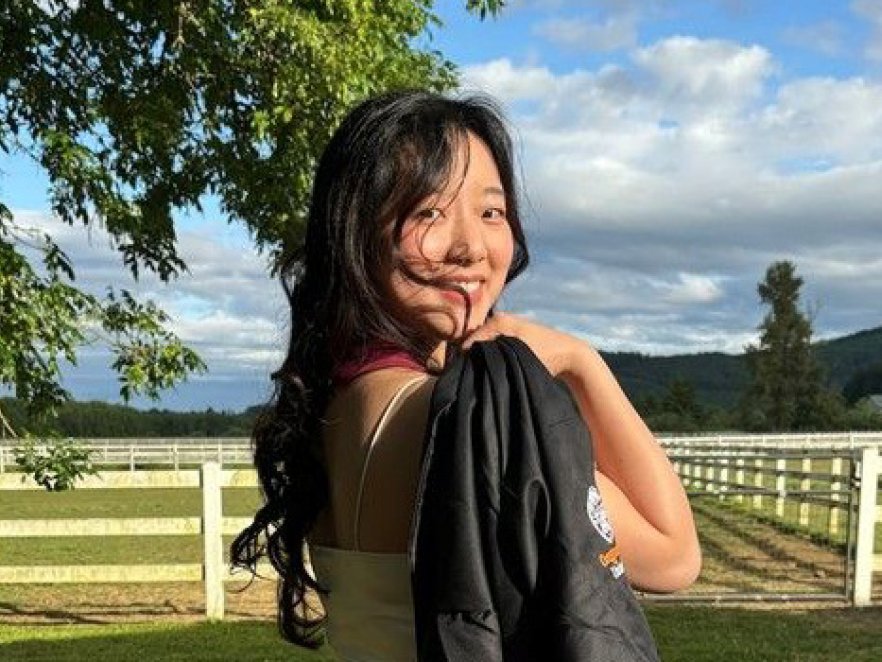 A smiling young woman holds her graduation gown on a sunny day