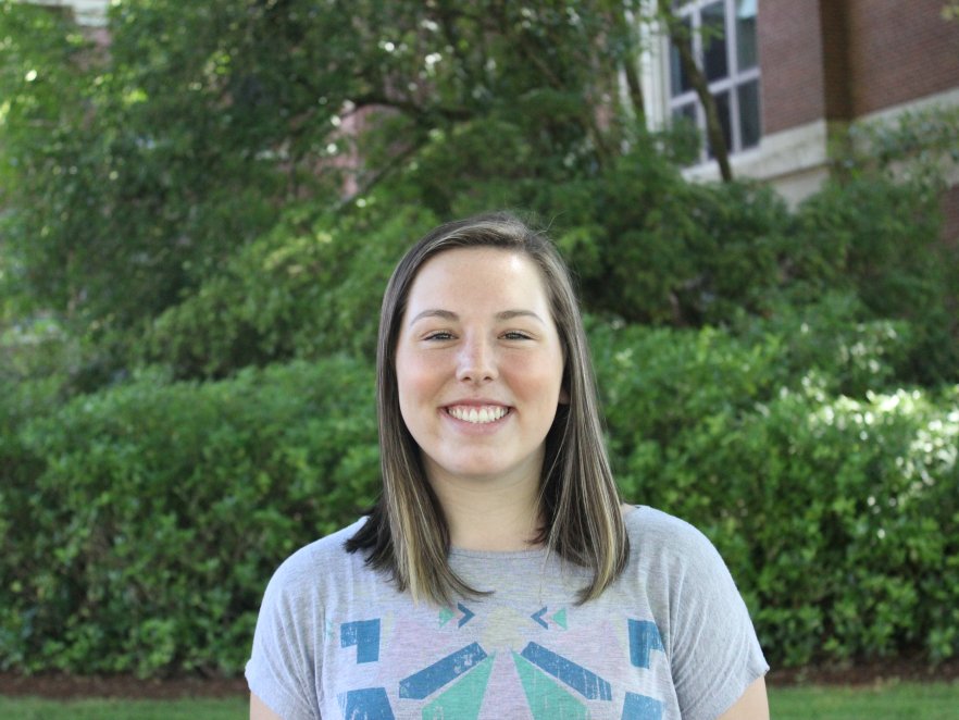 A young woman smiles on a vibrant green campus