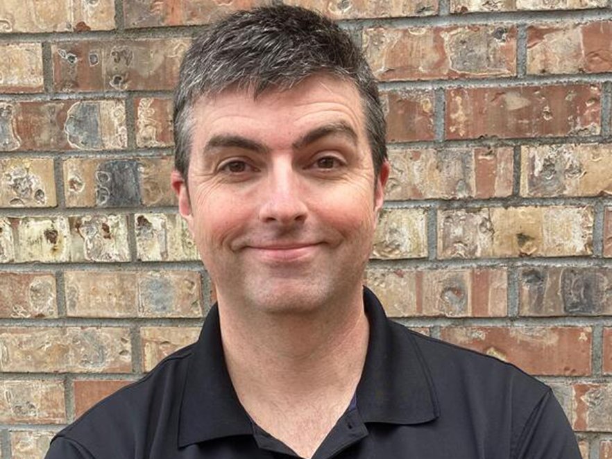 Smiling man standing in front of a brick wall